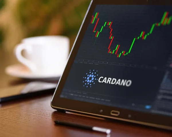 a smart phone on a table showing the stock chart or cardano. a coffee cup in the background on the table.