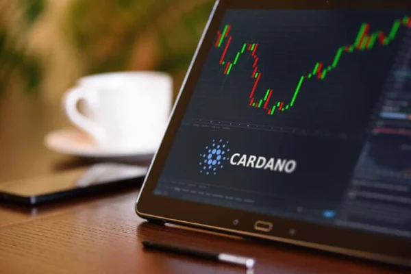 a smart phone on a table showing the stock chart or cardano. a coffee cup in the background on the table.